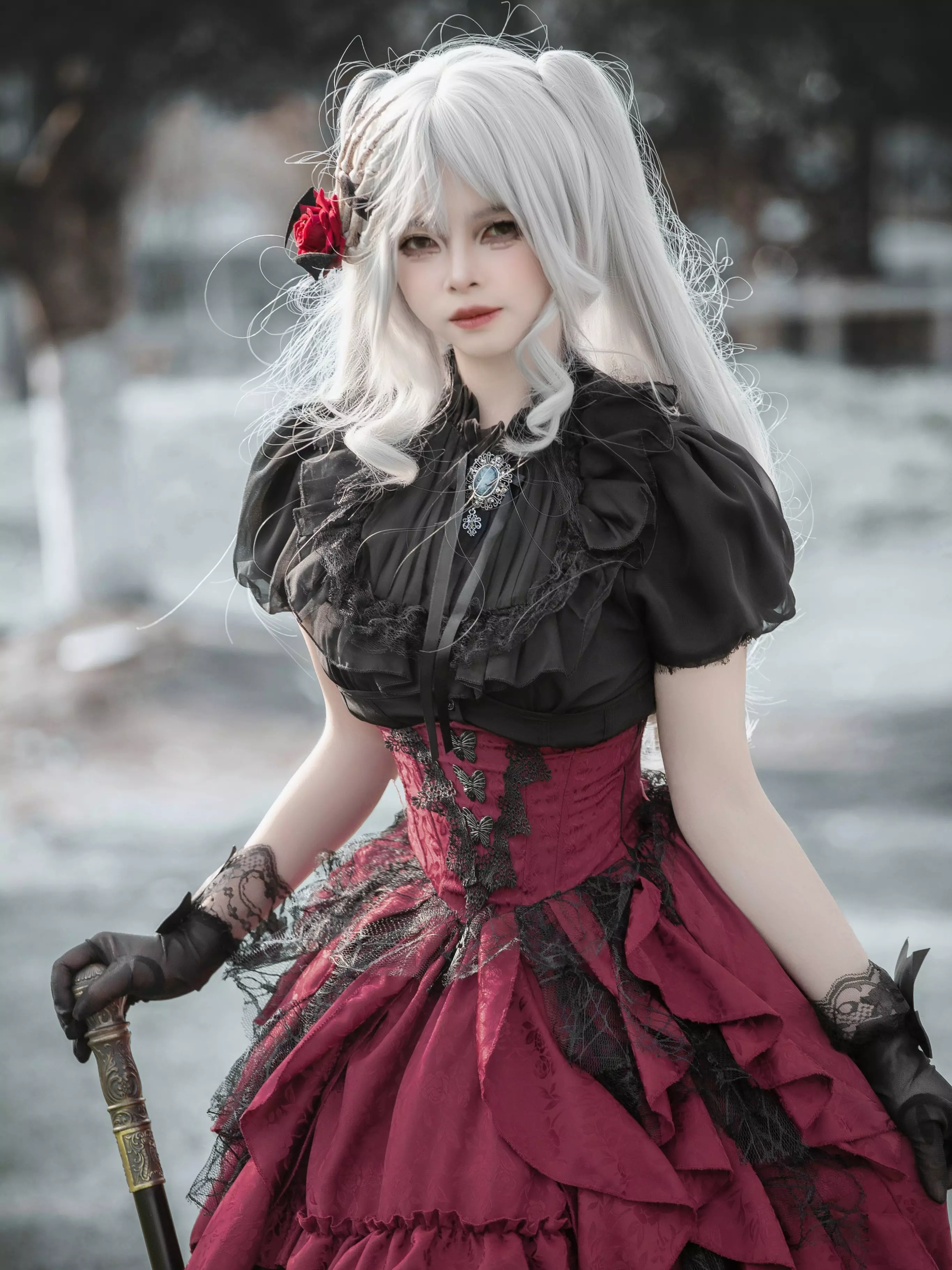 Close-up front detail of gothic lolita dress showing black lace puff-sleeve blouse with brooch, wine-red corset-style skirt with tiered ruffles, rose hairpin