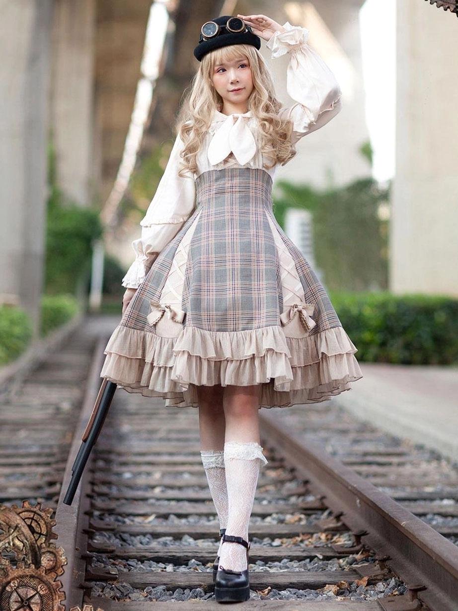 Camel classical Lolita JSK dress with bow details on blonde model in railway outdoor setting, showcasing front full-body view and plaid pattern tiered skirt