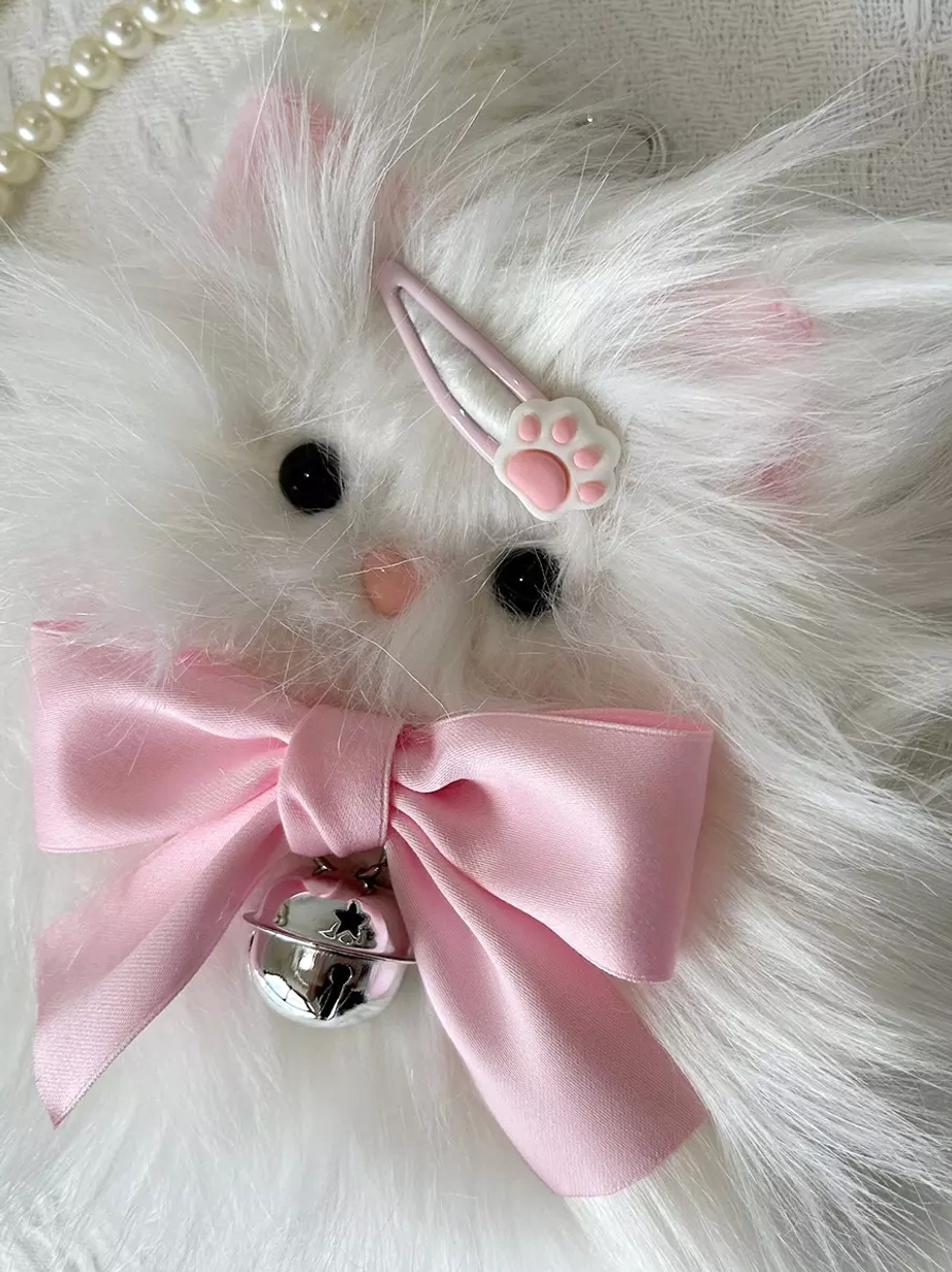 Extreme close-up of cat bag front face showing black button eyes, embroidered pink nose, large pink bow with silver bell, and paw-shaped hair clip detail