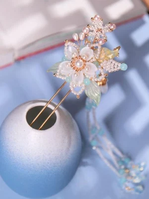 Chinese-inspired pearl tassel hairpin with white resin flowers and blue beaded cascading drops, displayed on blue ceramic holder with gold metal hardware – Lolita accessory collection detail view