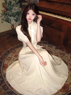 Beige vintage classic lolita midi dress with stand collar, lace flutter sleeves, and front chest bow brooch, shown on model in seated three-quarter front view highlighting the corset-inspired waist and full swing skirt silhouette