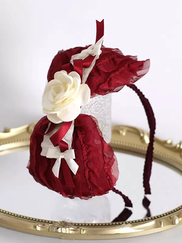 Romantic lolita hair accessory featuring wine red ruffled bows white roses and delicate details front view on glass stand with gold tray