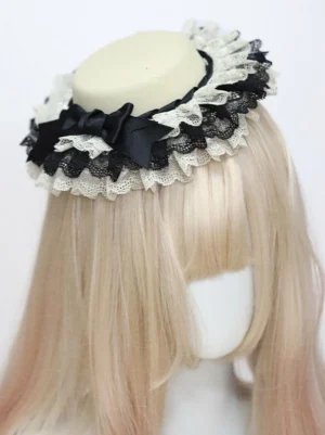 Classic Lolita mini top hat with beige crown and dual-tone ruffled lace trim featuring black satin bow, front three-quarter view on mannequin with blonde wig