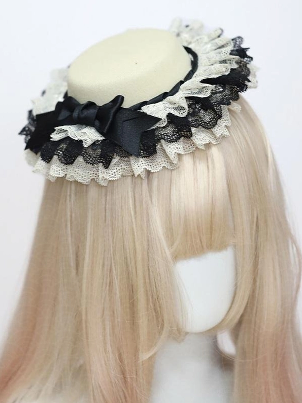 Classic Lolita mini top hat with beige crown and dual-tone ruffled lace trim featuring black satin bow, front three-quarter view on mannequin with blonde wig