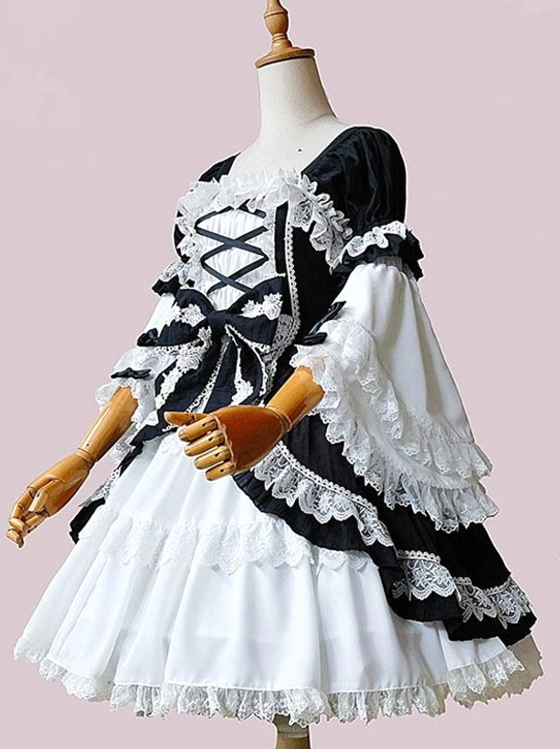Classic Lolita black and white one-piece dress with crisscross front lacing, layered lace ruffles, and statement black waist bow, displayed on wooden mannequin with three-quarter side view