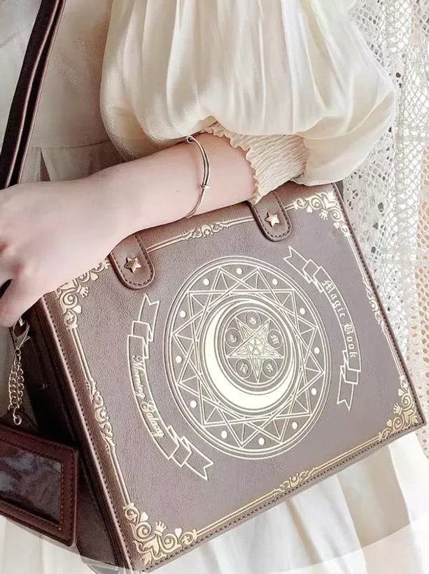 Coffee brown Gothic Lolita crossbody bag worn on wrist close-up with puffy white lace blouse, showing golden moon-star print and metal buckle details