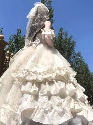 Cream fairy lolita gown rear side angle showing off-shoulder ruffle cuffs, layered frill skirt, and bridal veil in sunny outdoor setting