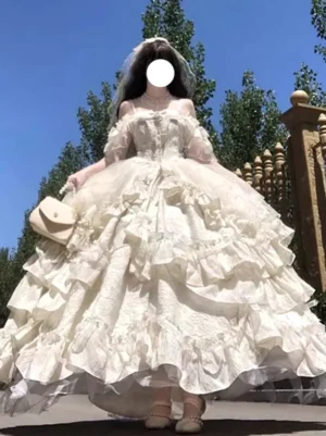 Cream off-shoulder fairy lolita wedding ball gown with tiered ruffle skirt, full front view outdoors with bridal veil and beige handbag accessory