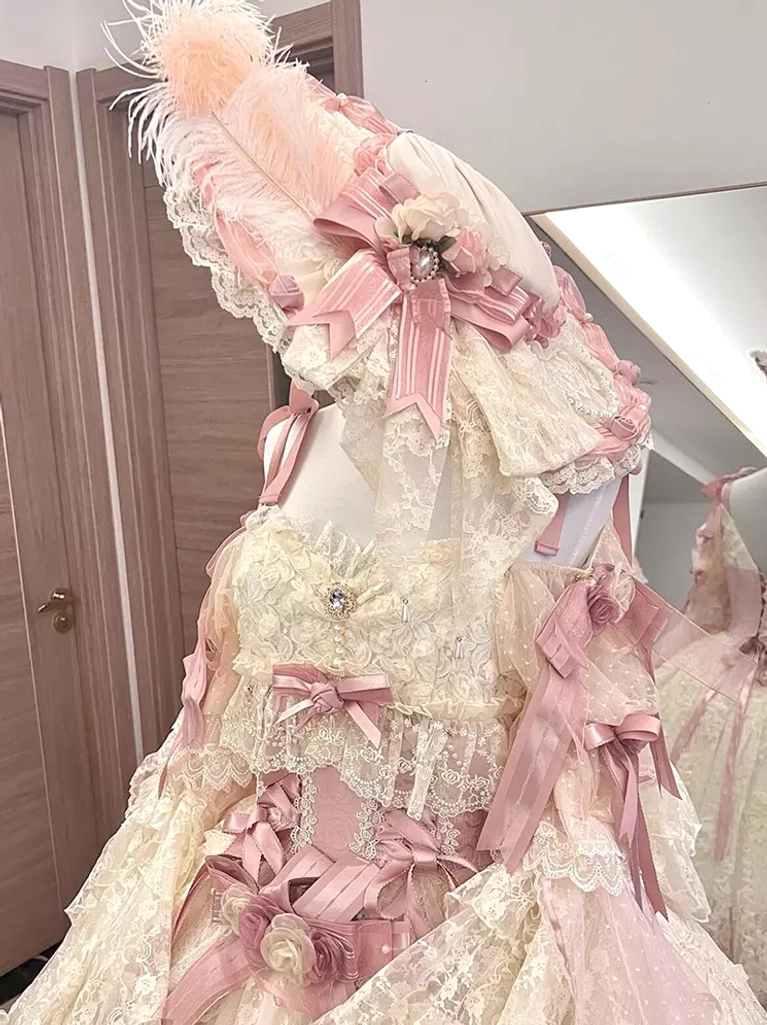 Cream pink lolita dress detail lace bustier multiple pink ribbon bows feathered headpiece close up view