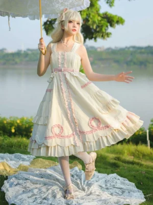 Cream sweet Lolita JSK jumper dress front view with pink ruffled trims, square neckline, sleeveless design, tiered flared skirt, worn outdoors at lakeside with lace parasol accessory