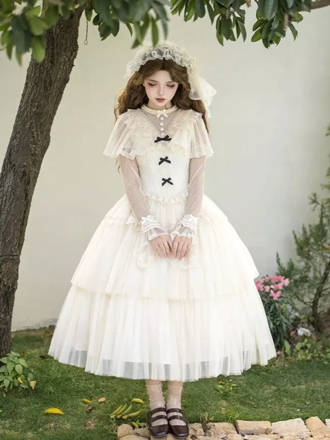 Full front view of cream white Lolita midi dress with high stand collar, three black bow trims on bodice, multi-layered tulle skirt, and lace headband on model in outdoor lawn