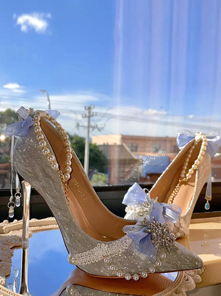 Back three-quarter outdoor view of glitter bridal stiletto pumps with dangling crystal decor pearl trim and clear high heel