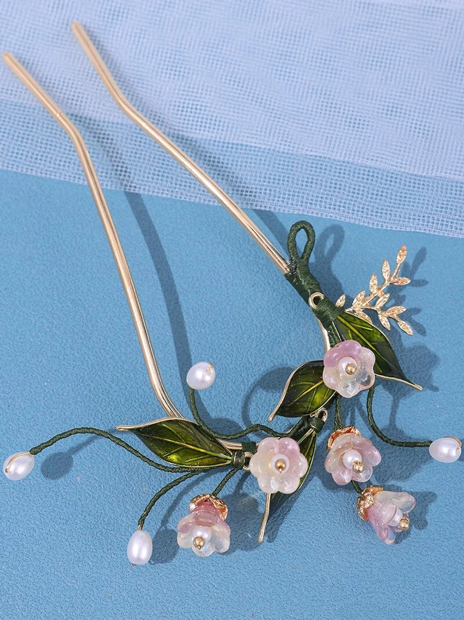 Curved floral hairpin headwear with abundant pink and green botanical elements and precious-looking pearl decorations on gold metal frame, side view on sheer blue fabric for classic lolita aesthetic