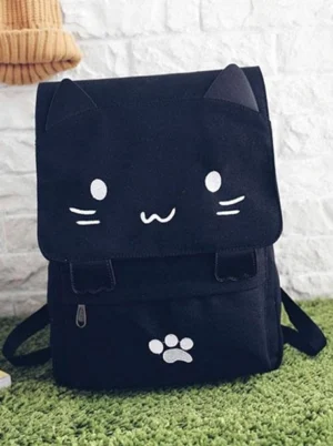 Cute black cat canvas lolita backpack front flat lay view with embroidered cat face and paw details on white brick wall with green turf background