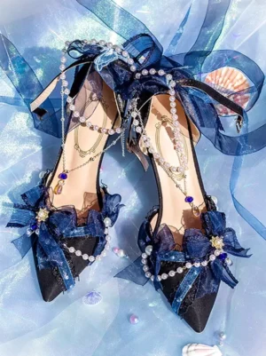 Dark blue Lolita bridal pointed heels with pearl trim and sheer bows, flat lay top-down view with blue satin and seashell backdrop