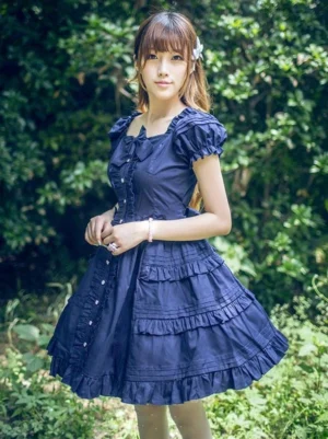 Dark navy blue classic lolita OP one-piece dress with puffed short sleeves, square neckline, layered tiered ruffled skirt, and front bow detail on model outdoors with green plant background