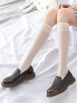 Side profile of ecru sheer lolita socks with rolled cuff and brown leather shoes on cozy bedding background