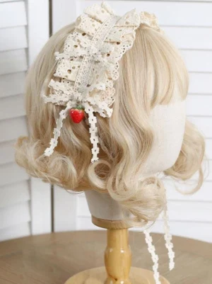 Ecru white lolita headdress with ruffled lace and red strawberry pendants shown from rear perspective on blonde curled wig mannequin, displaying back lace tassels and pastoral rococo design elements