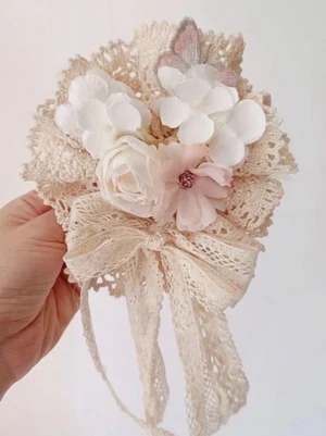Close-up frontal view of ecru sweet lolita hair clip with lace bow streamers hydrangea rose blooms embroidered butterfly ornament held in hand