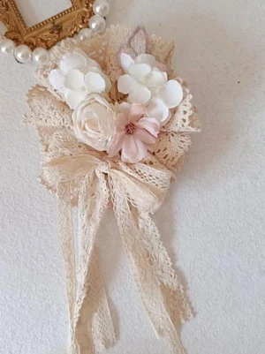 Ecru sweet lolita floral lace hair bow with pink white flowers and ruffles displayed on vintage pearl frame wall decor showing lace bow design with long streamers