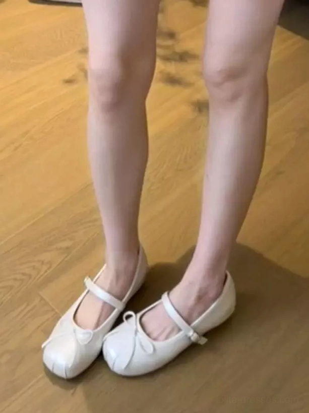 Ecru white ballet flat Mary Jane lolita shoes with bow front detail, showing oblique lower leg view of female model wearing the flats with elegant leg positioning