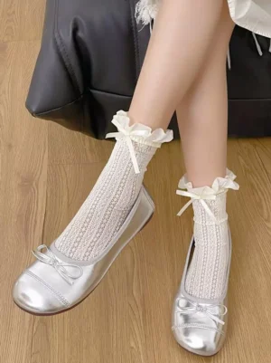 Ecru white sweet lolita ankle socks with ruffled cuffs and satin bow detail, worn on legs indoors with wooden floor background