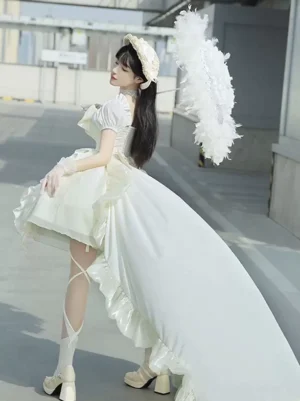 Ecru white sweet lolita dress with puff sleeves and ruffled bow worn by model in outdoor setting, showing rear side view of voluminous skirt and statement back bow detail