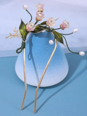 Emerald garden floral hair fork with pink resin flowers and green enamel leaves on gold metal prongs, displayed on blue gradient vase showing detailed top-down view of pearl beads and gold leaf accents for lolita tea party wear
