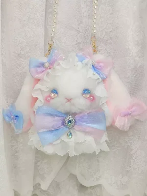 Enchanted bunny lolita crossbody bag front top-down view with white plush rabbit, gradient pink-blue rhinestone bow, ruffled lace trim, crystal eyes and blushed cheeks on lace backdrop