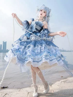 Enchanted fairytale sweet lolita dress in gradient deep blue organza - full-body front three-quarter view showing tiered ruffled skirt, off-shoulder ruffled sleeves, 3D floral bodice embellishments, and pearl chain accents worn on lakeside beach with blue-haired model