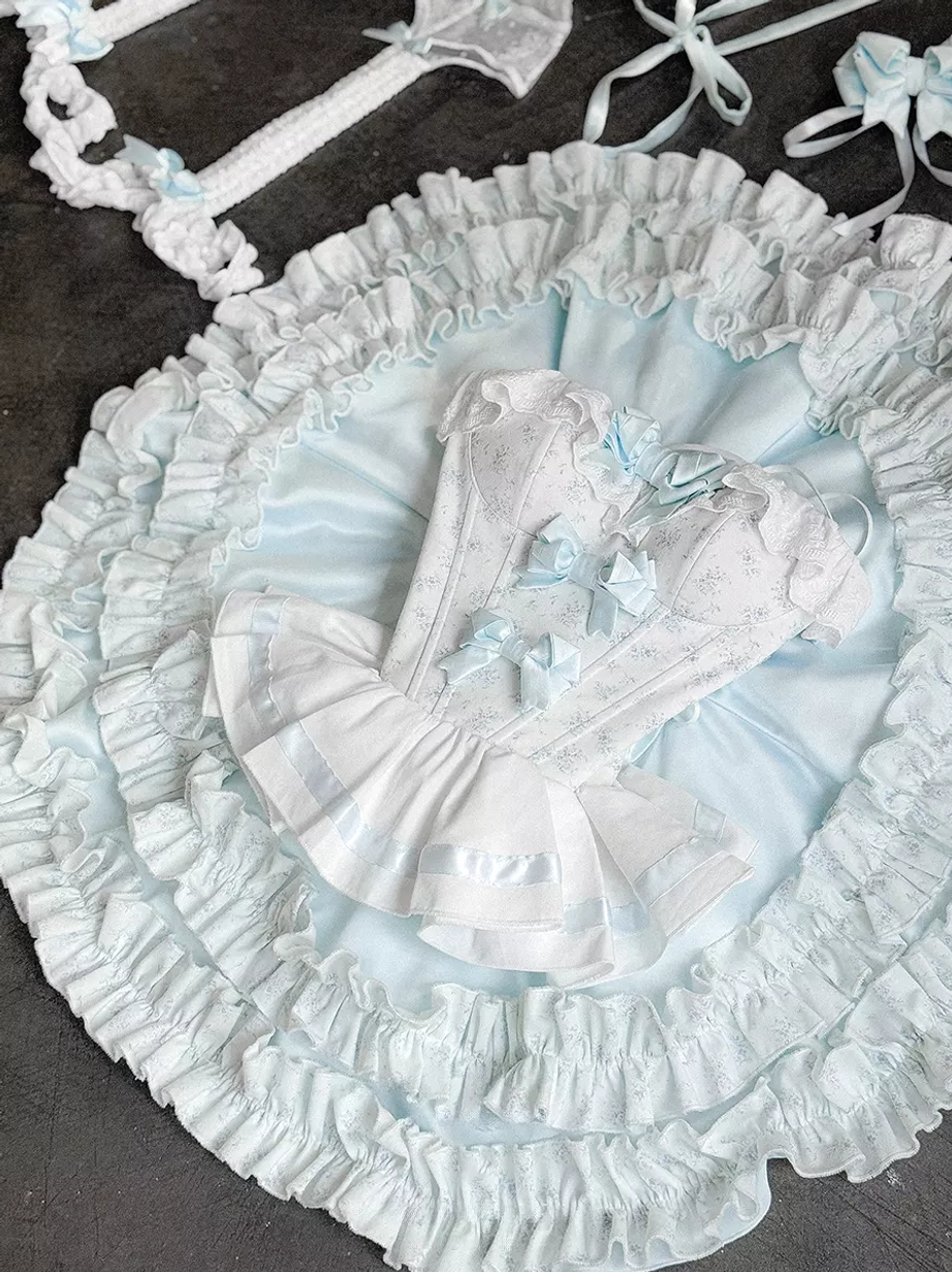 Fairy lolita dress set flat lay top-down view on dark tabletop showing complete ensemble tiered ruffled skirt matching bow accessories