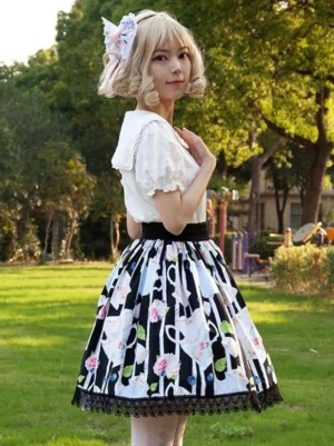 Black floral print lolita skirt with delicate tea cup motifs, side three-quarter angle displaying layered ruffles and high-waist design, paired with white puff-sleeve blouse in garden setting