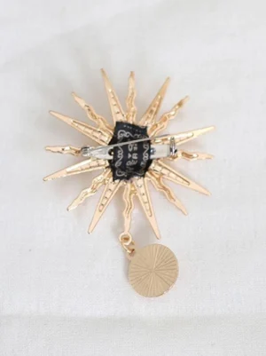 Gold sunburst brooch accessory with hanging round disc charm and safety pin backing - flat lay rear view on white fabric background, Lolita hat decoration detail