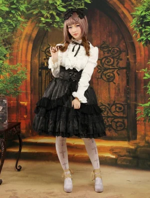 Gothic black jacquard lolita skirt full front view with white ruffled blouse, cross patterned stockings, and platform shoes in vintage European courtyard setting