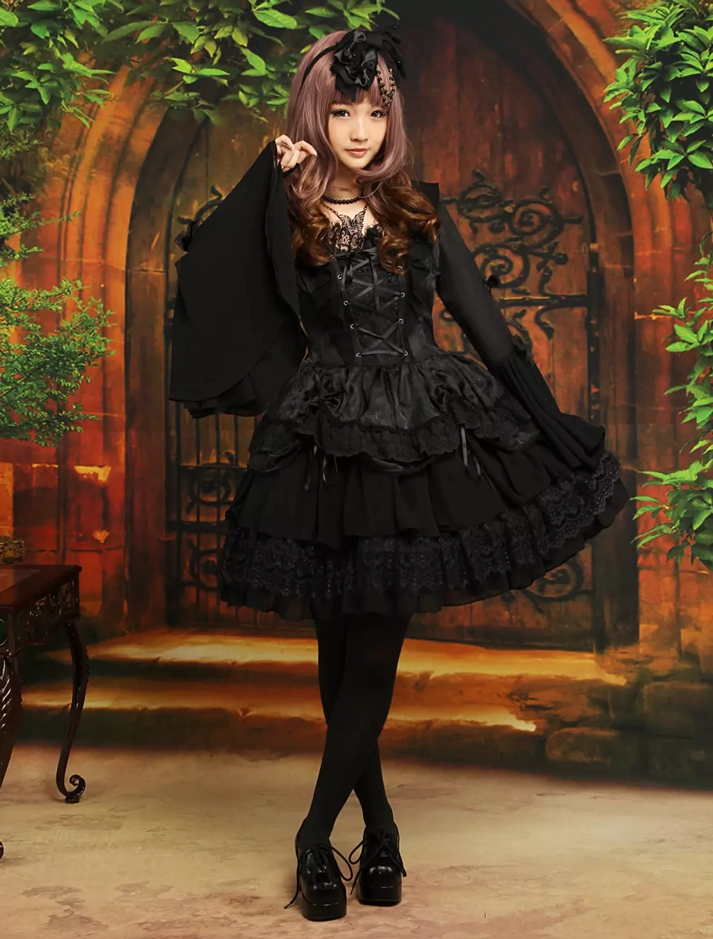 Full front view of gothic black lolita dress on model wearing black tights and platform loafers, displaying dramatic flare sleeves and multi-tier ruffled lace skirt