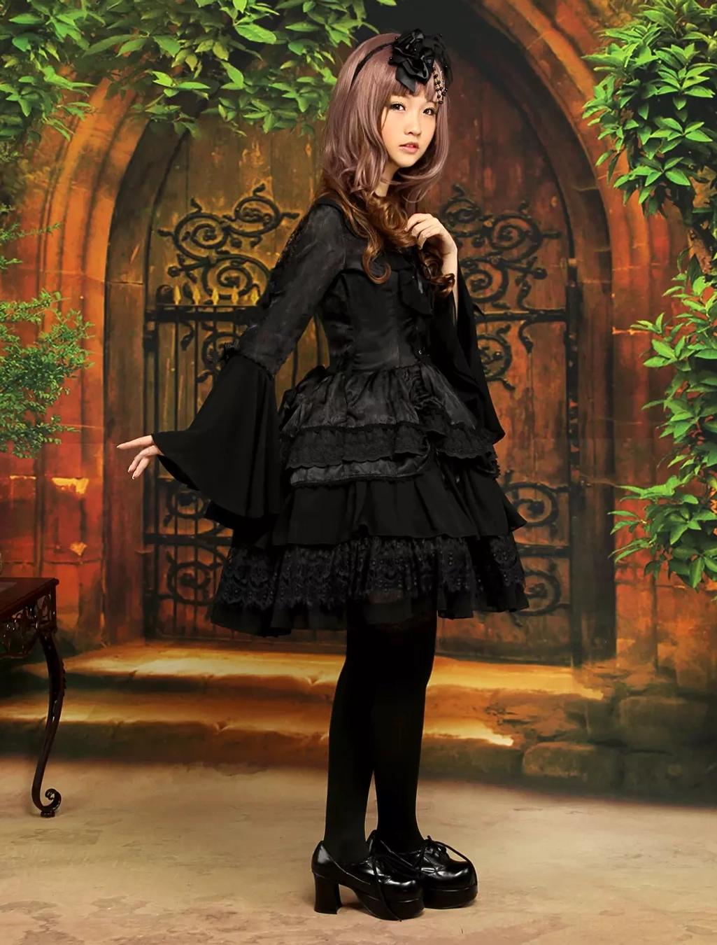 Left side full view of gothic black lolita dress on model with hand posed elegantly, showcasing corset-style front and layered ruffled skirt silhouette