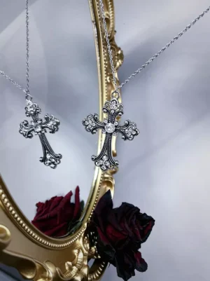 Gothic cross pendant necklace with clear rhinestone accents on silver tone alloy, displayed on ornate gold mirror with dried red roses, featuring intricate carved retro texture design perfect for lolita fashion