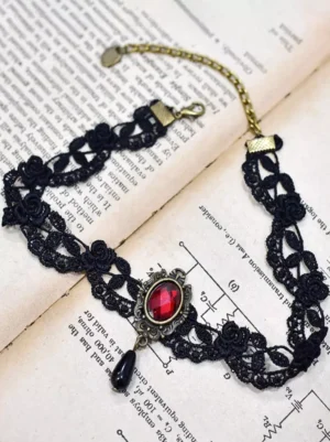 Vintage gothic black lace choker with adjustable extension chain displayed on antique book pages, oblique top-down view highlighting rose motif lace and bronze metal fittings