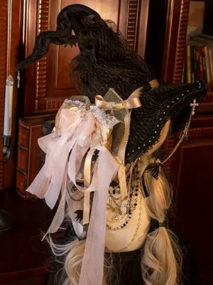 Gothic lace witch hat with pink-white ribbon bow and cross chain ornament on mannequin with blonde twin curly hair, back three-quarter view vintage lolita headdress