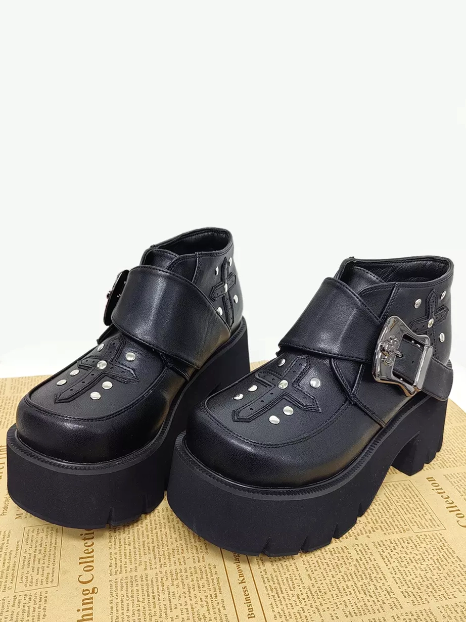 Front three-quarter view of gothic lolita ankle boots on textured newspaper background, showcasing thick platform outsole and rivet cross patterns