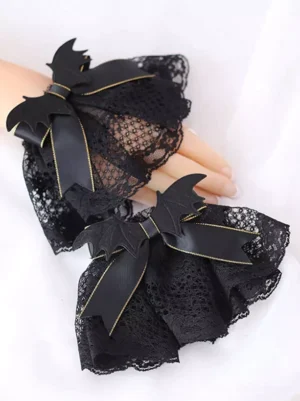 Close-up side view of gothic Lolita wrist oversleeves showcasing black lace fabric, black satin bows with gold edge trim, and decorative bat wing details on soft white background