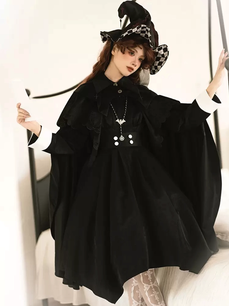 Black Gothic Lolita sleeveless cloak cape with layered ruffle collar worn by model in bedroom setting with witch hat, showcasing contrast white cuffs and waist button embellishments
