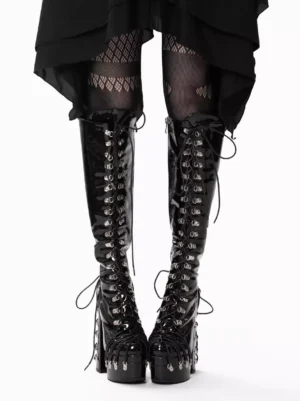 Gothic Lolita black patent leather platform boots front view with lace-up grommet details worn with fishnet stockings and asymmetric black skirt