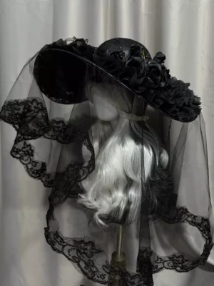 Gothic Lolita black wide-brimmed hat with lace-trimmed veil and black floral brim decorations, left front three-quarter view on mannequin with silver-white hair