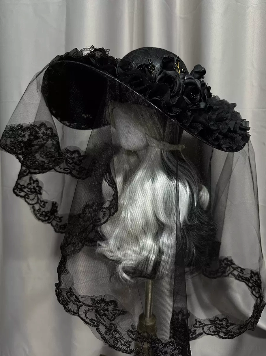 Gothic Lolita black wide-brimmed hat with lace-trimmed veil and black floral brim decorations, left front three-quarter view on mannequin with silver-white hair