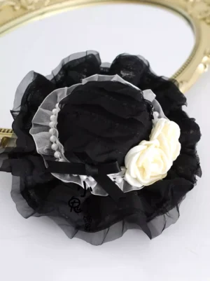 Gothic lolita mini bonnet oblique top-down angle displaying black satin bow detail pearl organza ribbon band and decorative rose lace elements against vintage gold mirror backdrop