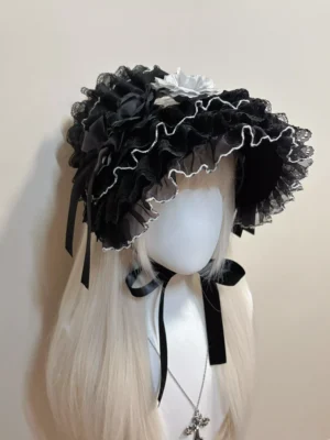 Black Gothic Lolita bonnet headdress with white lace ruffles and satin bows, displayed on white long-haired mannequin with cross pendant necklace, three-quarter left view showing intricate lace detailing and flower ornaments