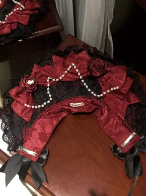 Gothic Lolita pearl chain bonnet hat with black lace base, wine red silk bows and rose ornaments, flat lay photography on wooden table surface