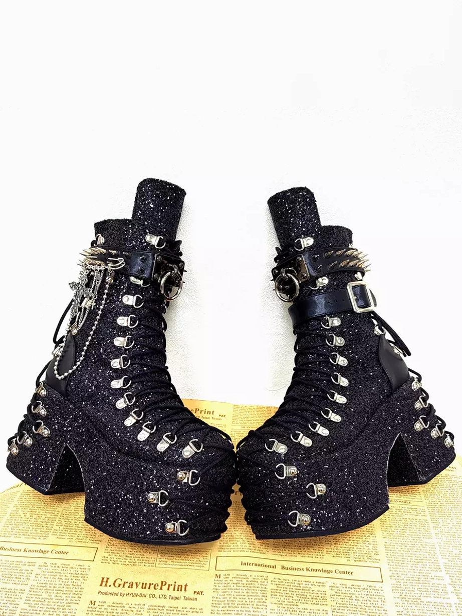 Gothic lolita platform boots front oblique view with mixed buckle straps, silver grommets, black glitter fabric upper, and prominent chunky platform heel silhouette
