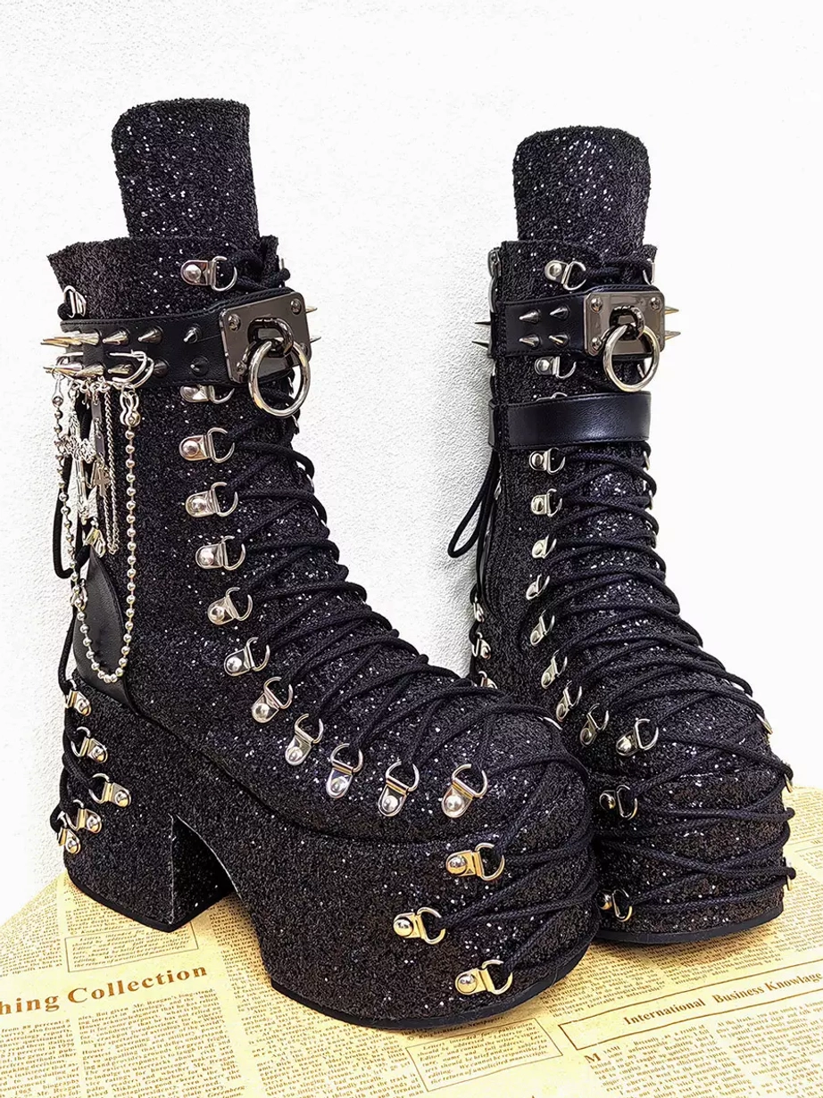 Gothic lolita platform boots on newspaper background showing decorative metal chain charms, black laces, silver grommets, and chunky platform heel side oblique angle